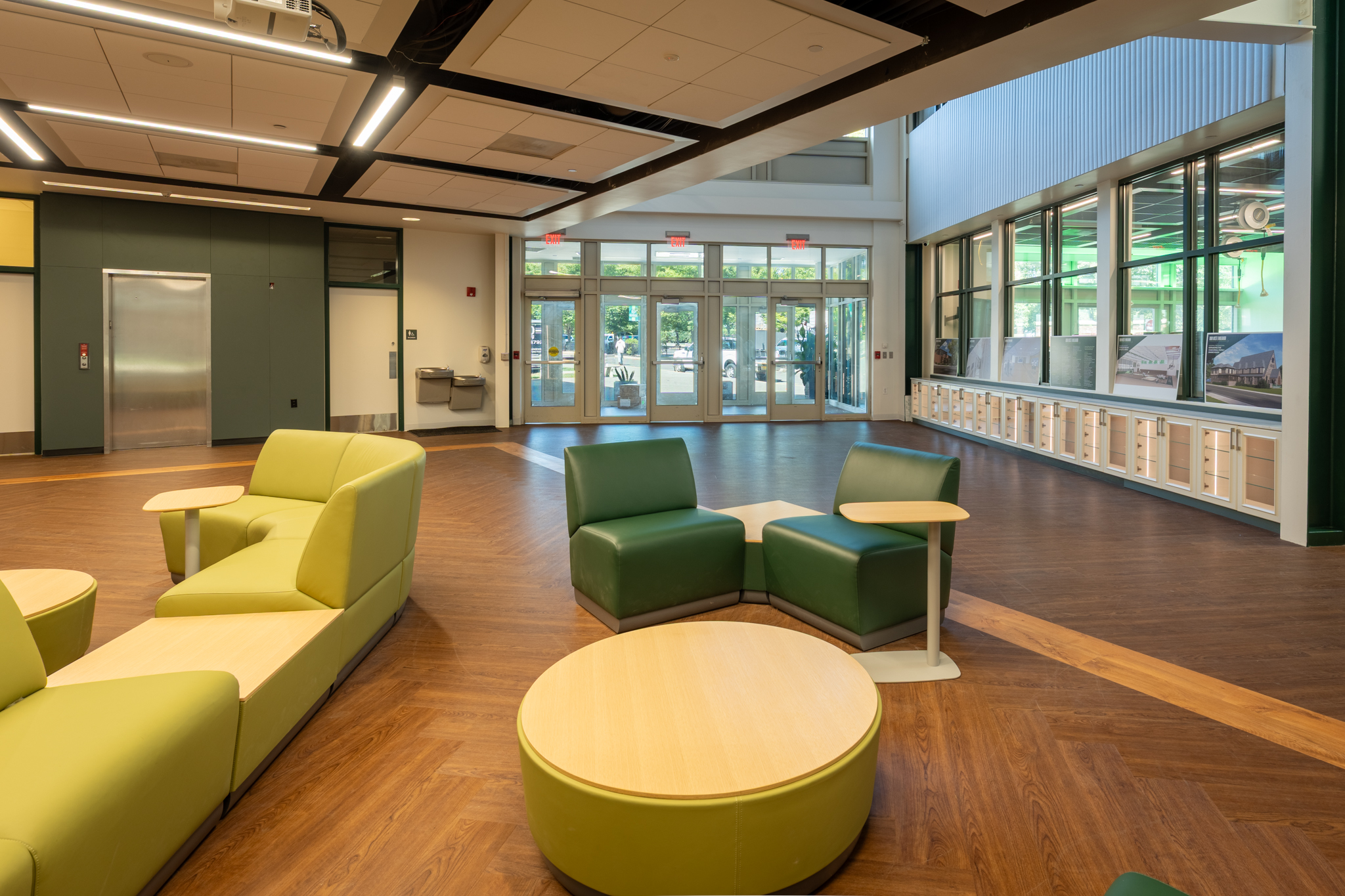 Bright school common area with green and yellow collaborative seating, wood flooring, and large windows