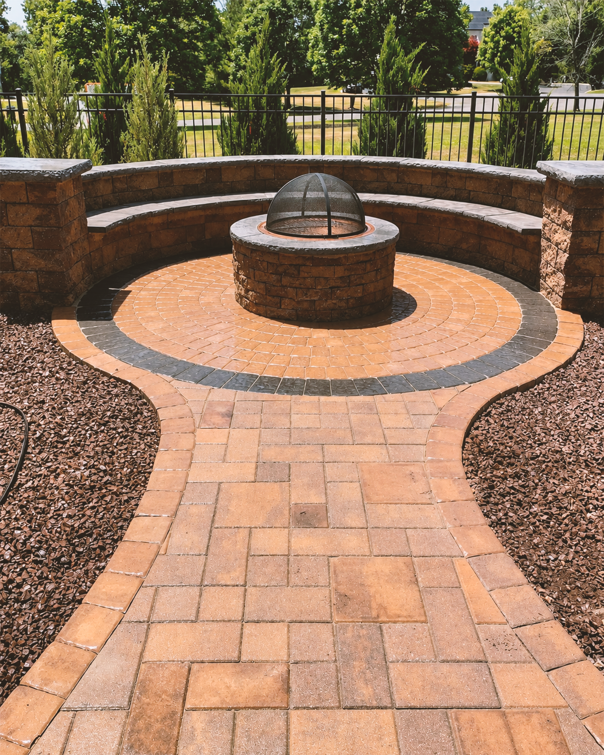 Circular masonry firepit with a curved seating wall and patterned paver walkway