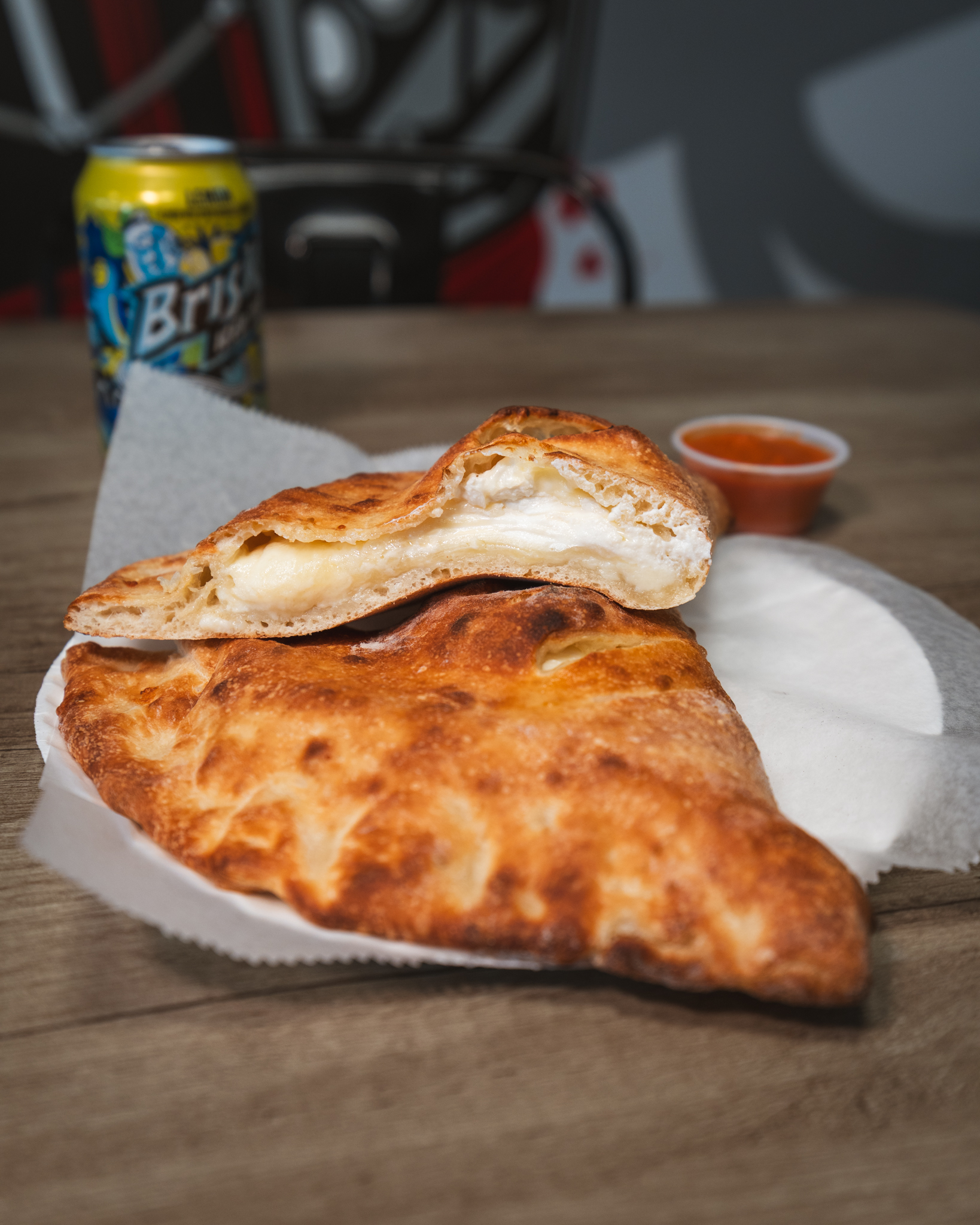 A golden baked calzone sliced open beside a cup of tomato sauce