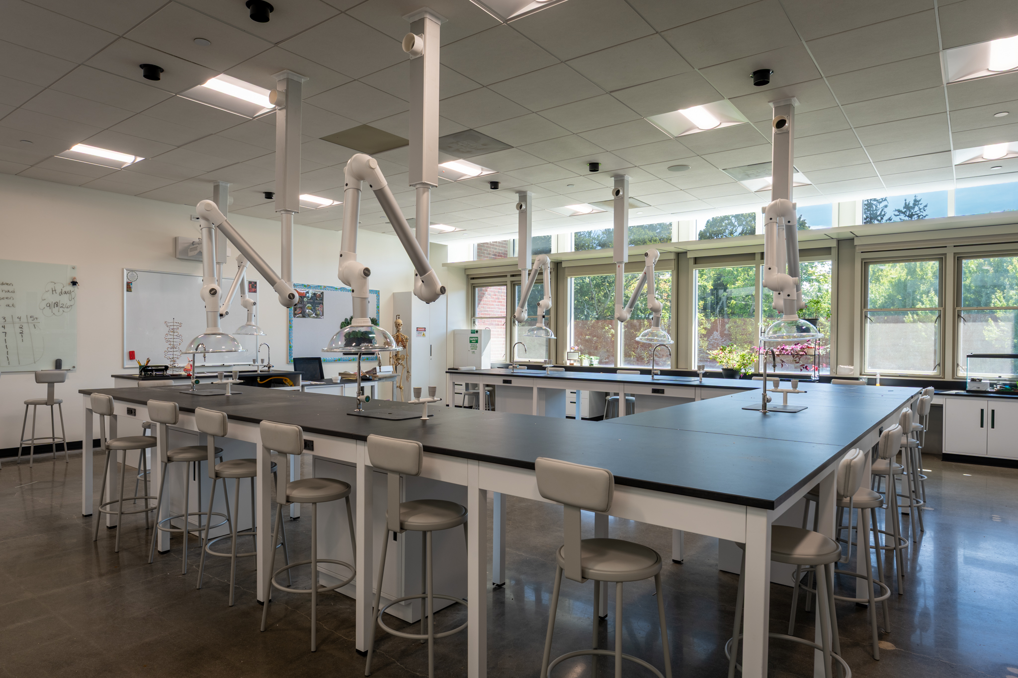 Completed science laboratory with black workbenches, white stools, and overhead extraction equipment