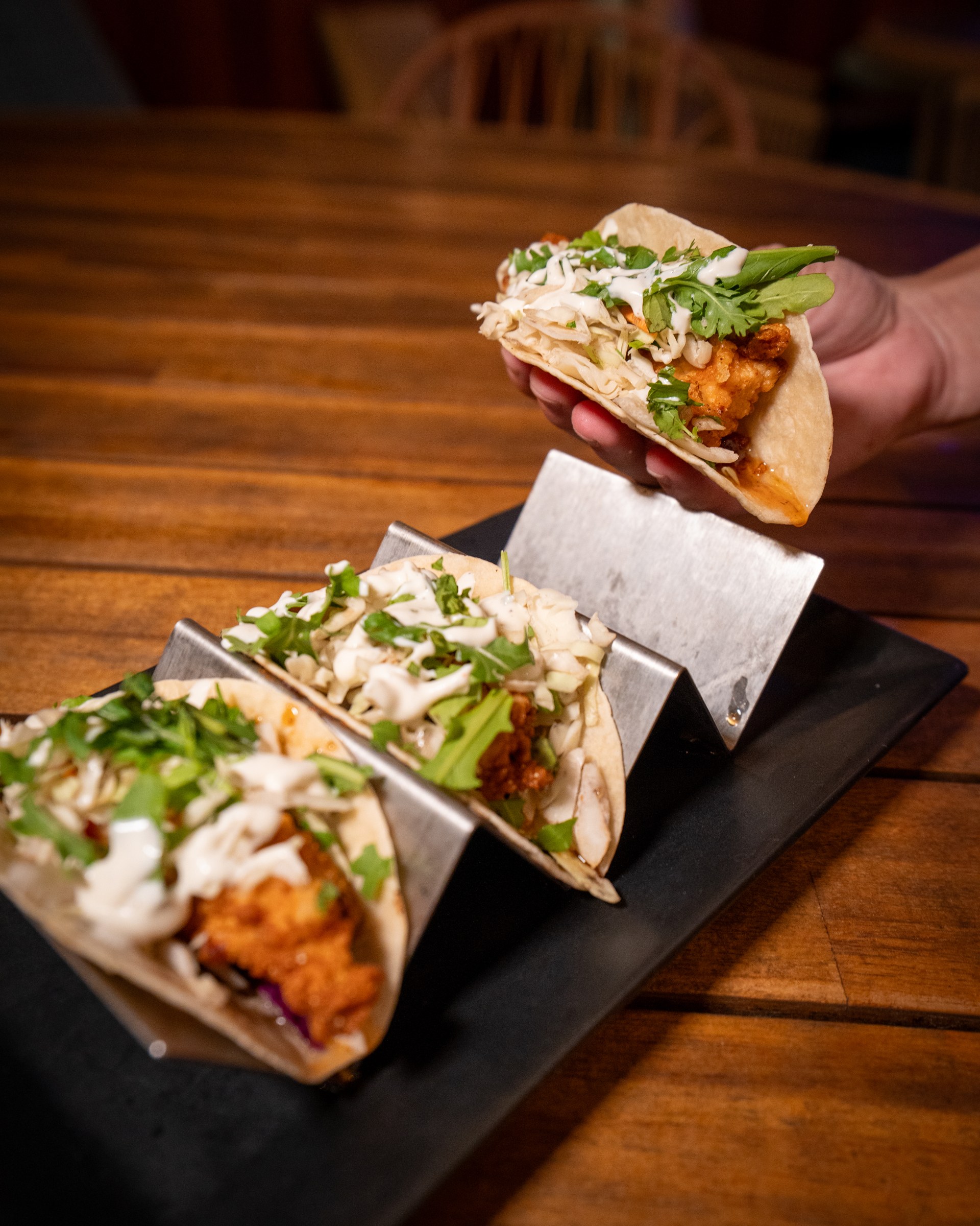 A hand lifting a taco above a tray of freshly prepared tacos
