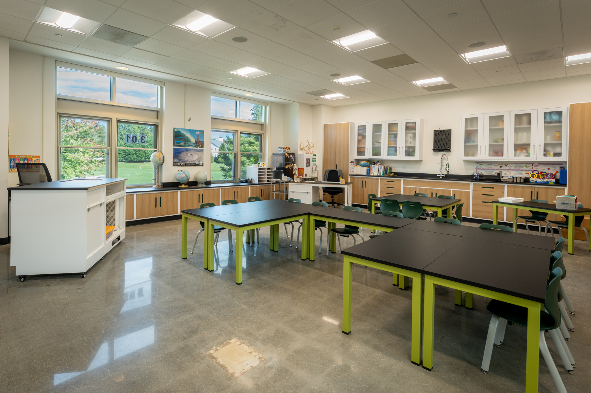 Science and making classroom with green-legged worktables, perimeter counters, and daylight from large windows