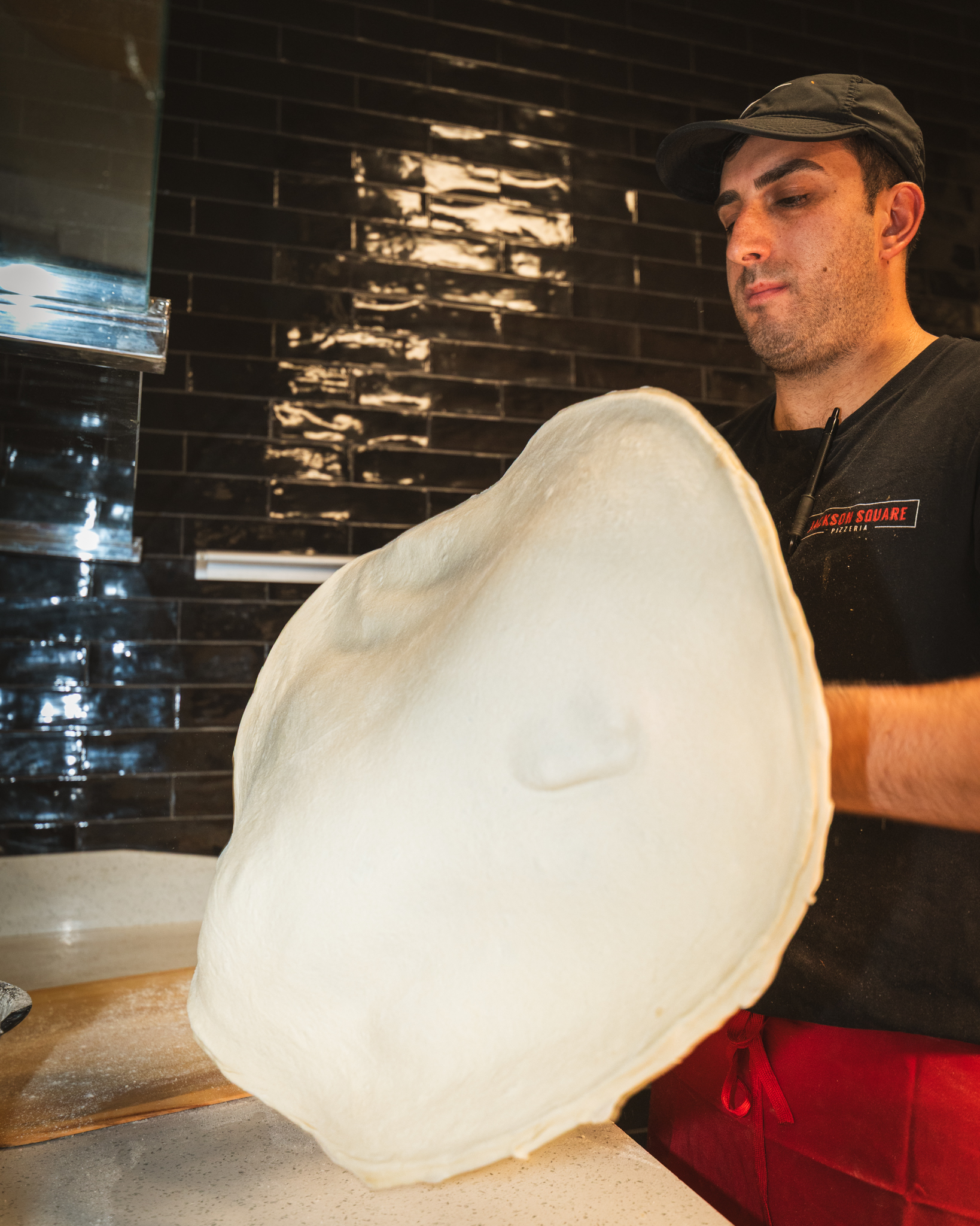 A pizza maker stretching a broad round of fresh dough in the Jackson Square kitchen
