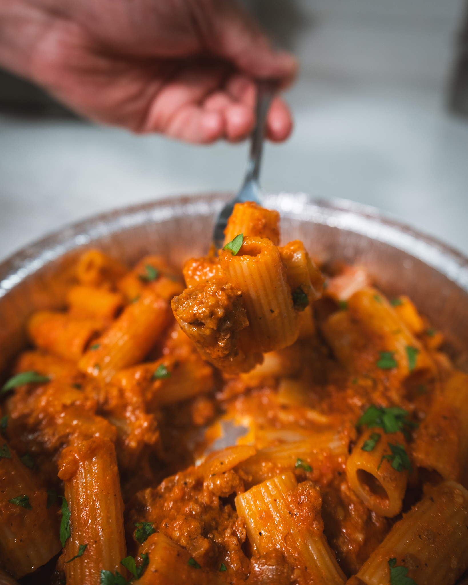 A fork lifting rigatoni coated in sauce from a freshly prepared pasta dish