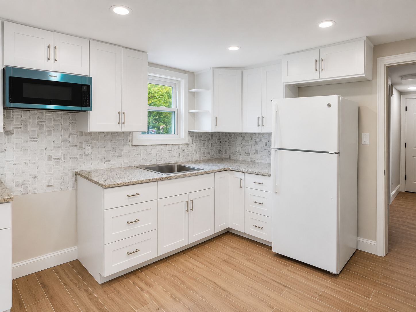 Bright kitchen with white cabinetry, a patterned backsplash and wood-look flooring
