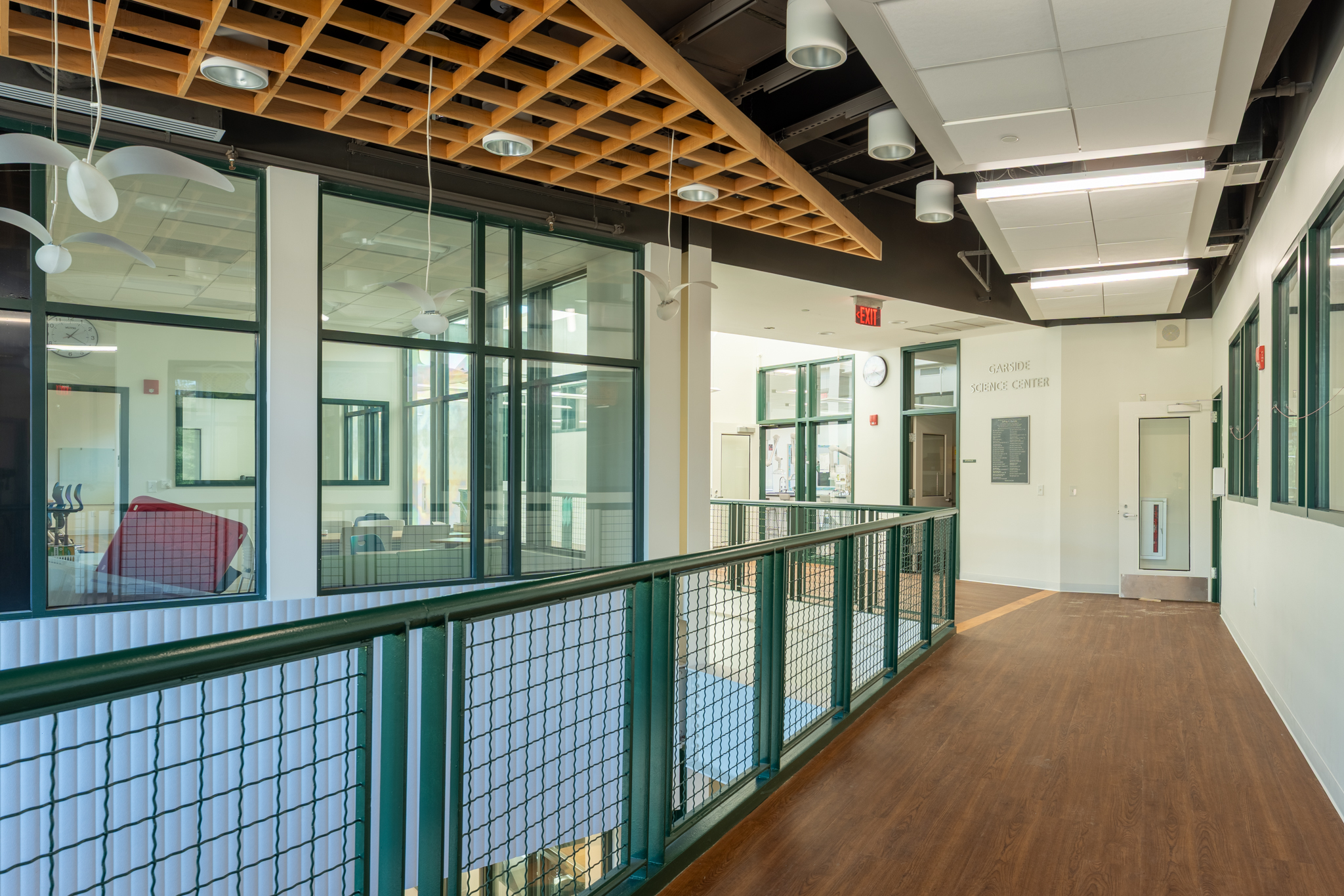 Glass-lined school circulation space with green railings, wood flooring, and an exposed timber ceiling