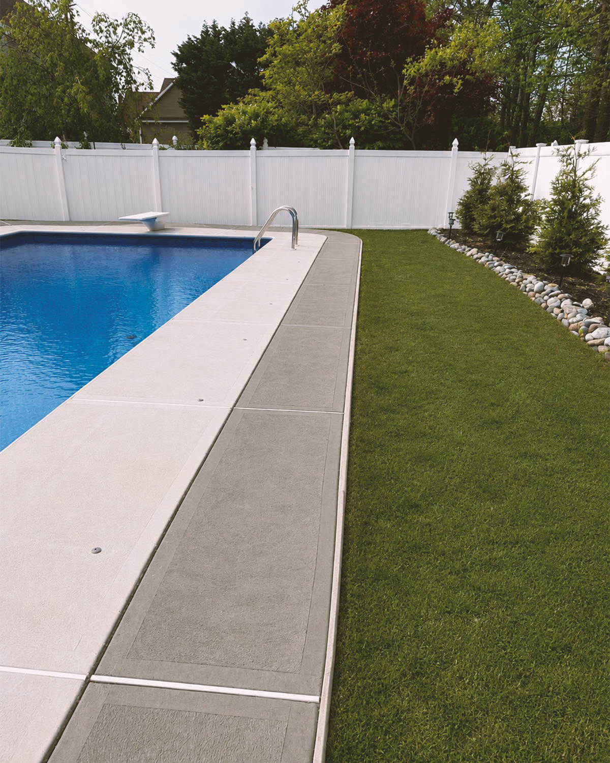 Swimming pool edged with concrete paving alongside a lawn and white fence